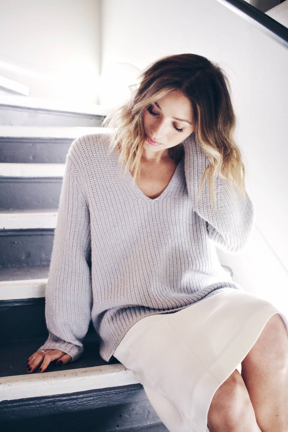moody photoshoot on stairs white midi skirt, oversized v neck sweater